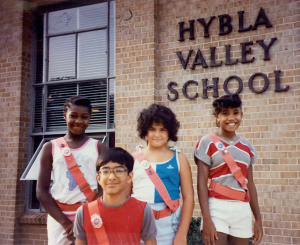 Color photograph of four students taken in September 1985. The students are part of the Safety Patrol and are wearing bright orange sashes and belts. They are standing in front of our building, near the old cafeteria, and the name of our school is visible above them on the right. 